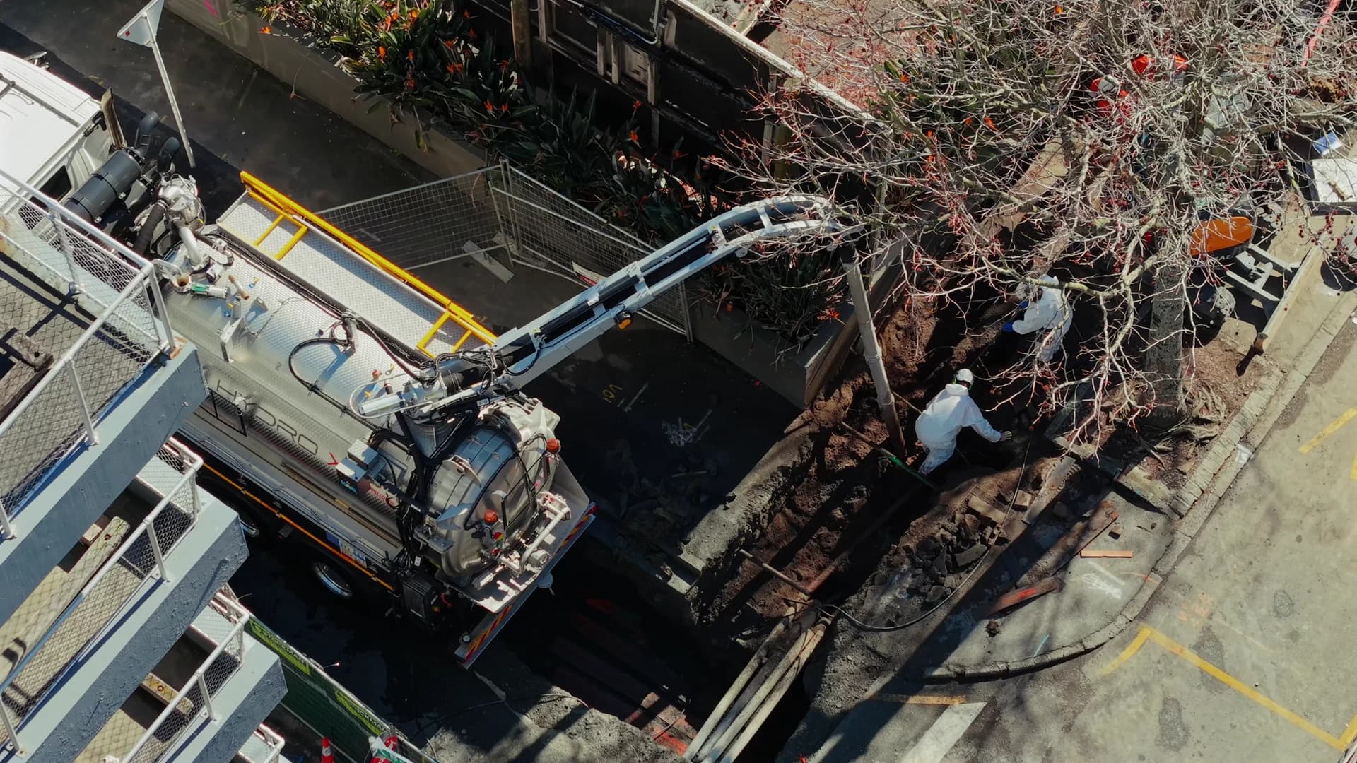 Truck boom over a roadside dig from above, crew in the excavation